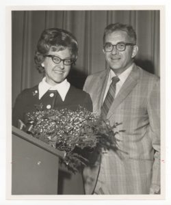 Pat Clapp and her husband standing behind a podium with flowers on it