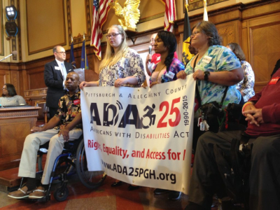 A group of people, one using a wheelchair, holding an ADA 25th anniversary banner