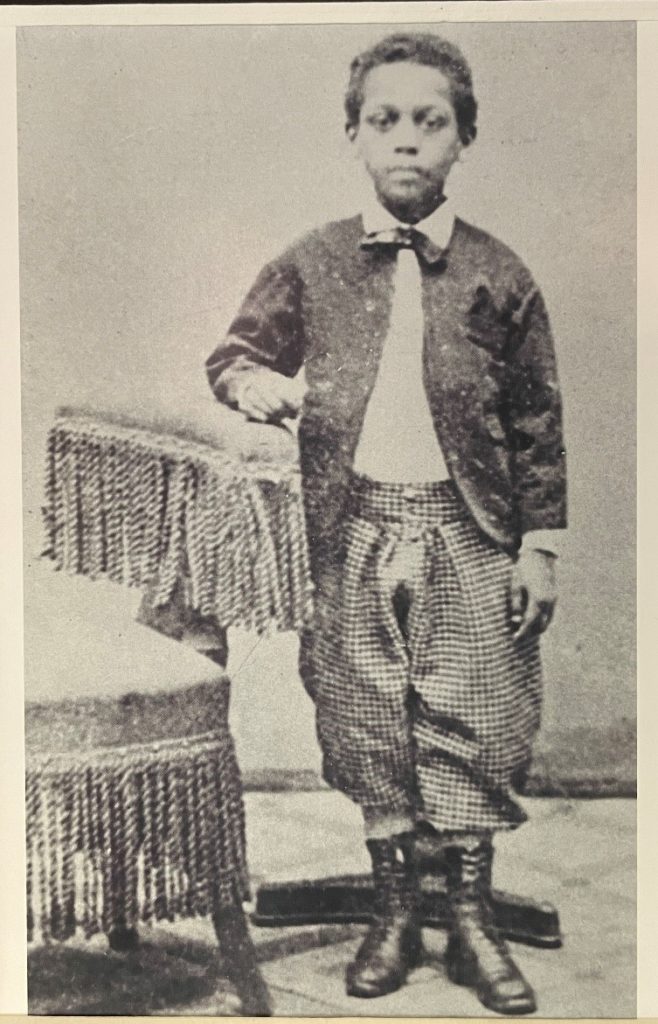 Henry C. Bell, a young Black boy standing near a chair