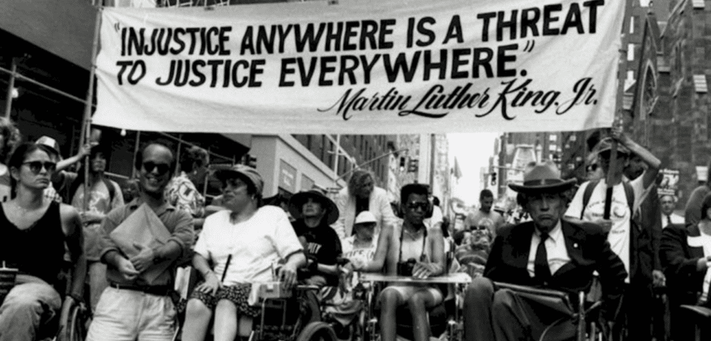 A crowd holding up a banner that says "Injustice anywhere is a treat to justice everywhere" by MLK