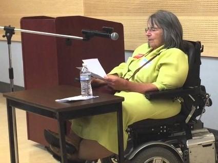 Judy Barricella giving a speech, seated in a wheelchair