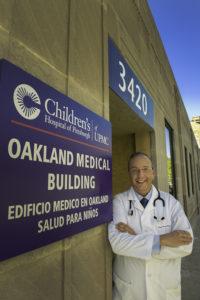 Dr. Chaves-Gnecco standing in front of a Children's Hospital sign wearing white lab coat and stethoscope.