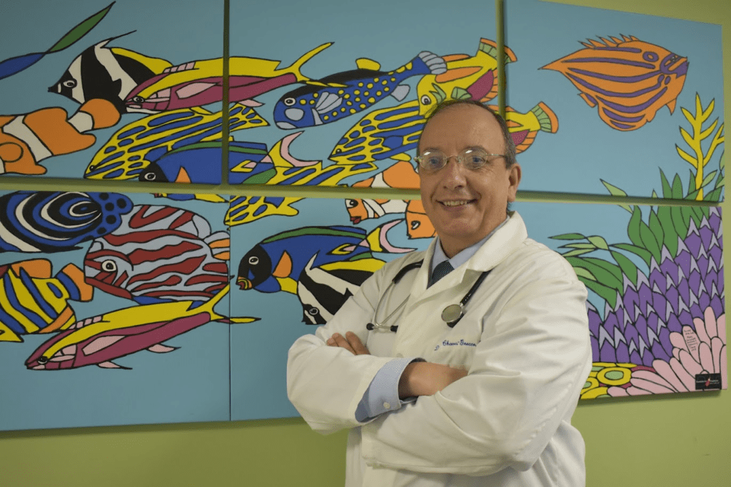 Dr. Chaves-Gnecco standing in front of a fish painting wearing white lab coat and stethoscope.
