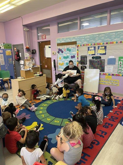 Head start classroom full of small children and a teacher reading to them