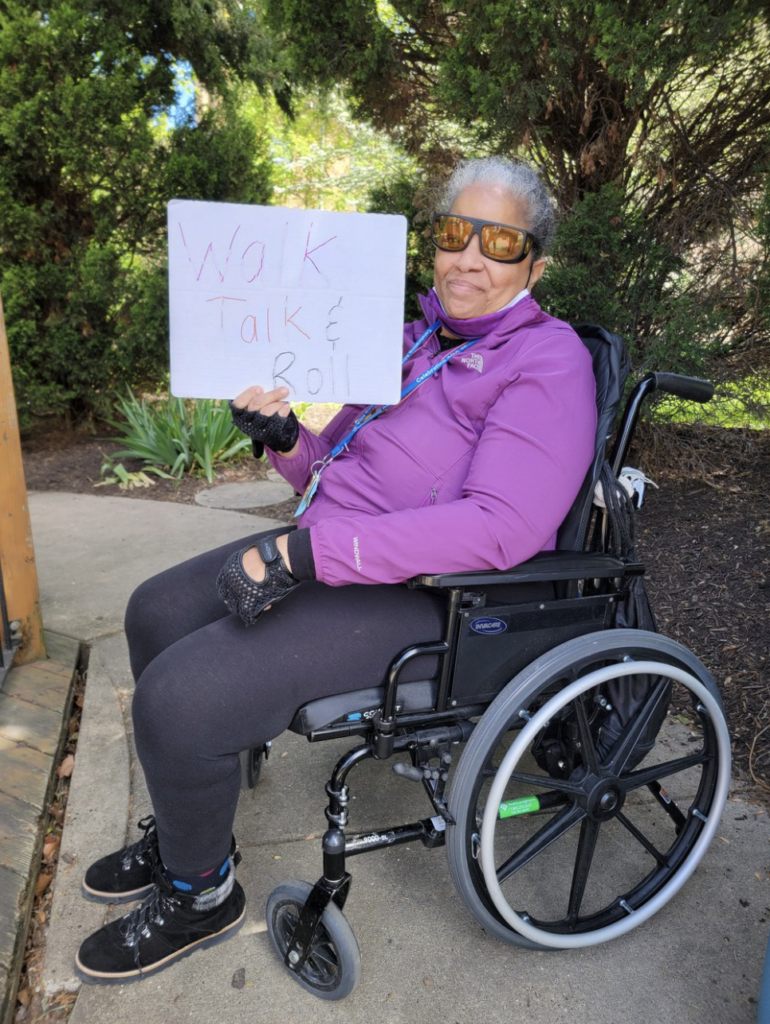Andrea Coleman Betts holding a Walk Talk and Roll sign while using her wheelchair