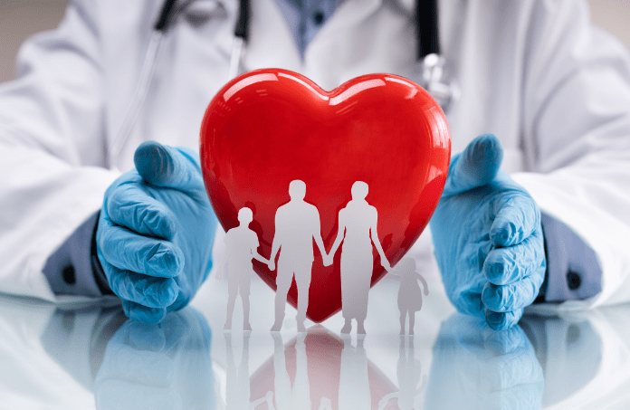 A doctor with gloved hands holding a heart with a cutout family in front of it