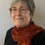 Head shot of Tina Calabro, a white woman with short salt-and-pepper hair, wearing eyeglasses, a black top with a red scarf