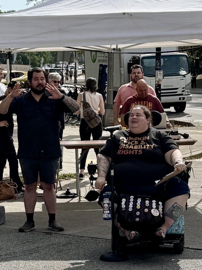 Alisa Grishman speaking at the event, there are numerous people behind her.