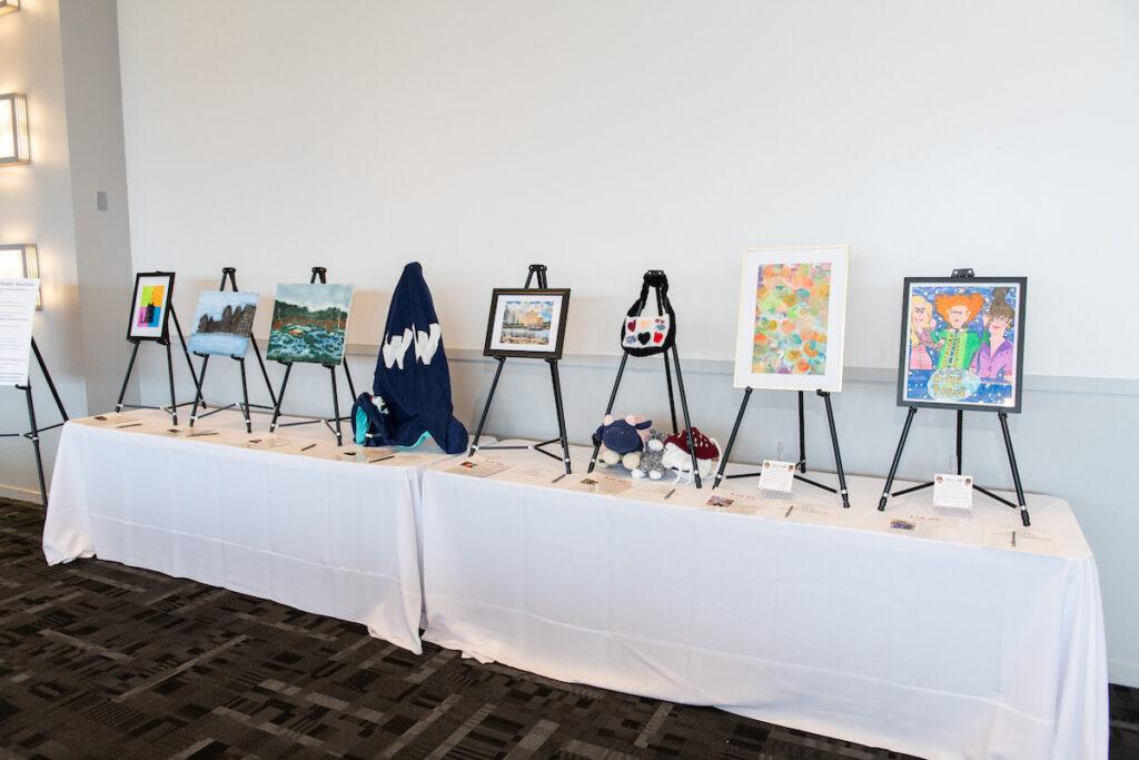The silent art auction table with easels, paintings, and maker items.