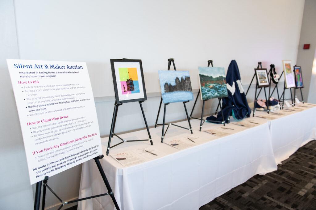 The silent art auction table with easels, paintings, and maker items.