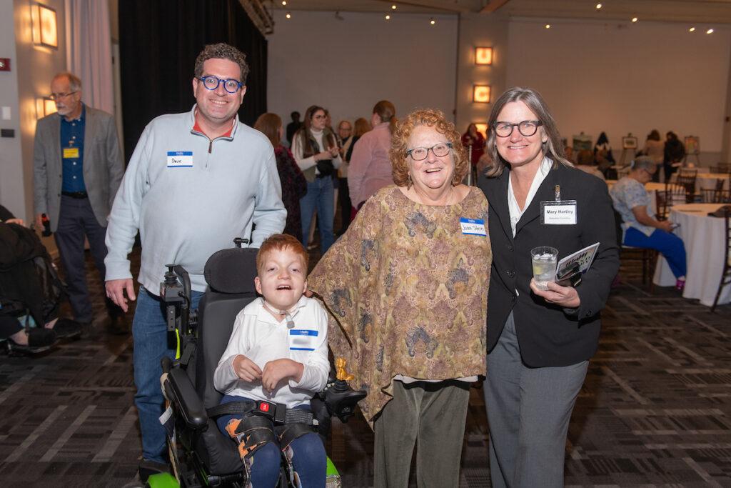 Two woman, a man, and a young boy using a wheelchair pose for a photo.
