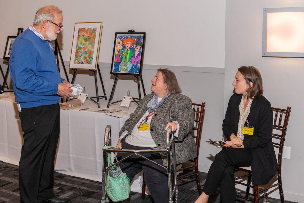 Silent auction volunteers talking to a guest.