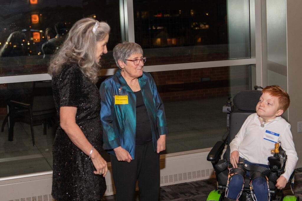 A young boy using a wheelchair talking to Ann Talman and Tina Calabro.