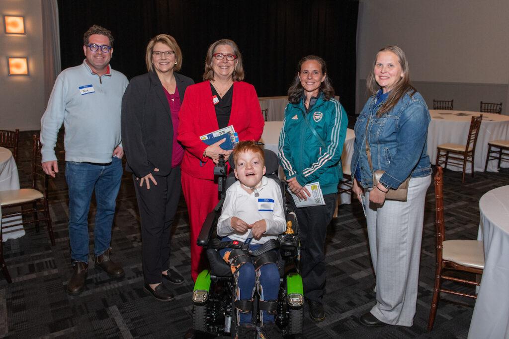 A group of guests posing for a photo - four women, one man, and a young boy using a wheelchair.